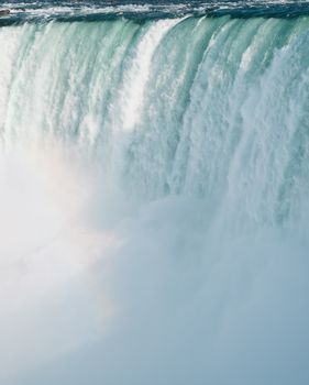 Stunning view of a large waterfall cascading with mist and forming a subtle rainbow.