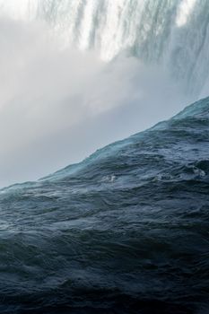 Powerful waterfall cascading over rocks with dramatic blue waves below.