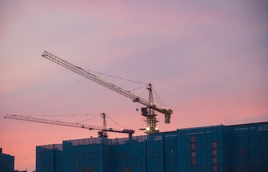 Construction cranes tower over a city skyline at sunset, symbolizing urban growth.