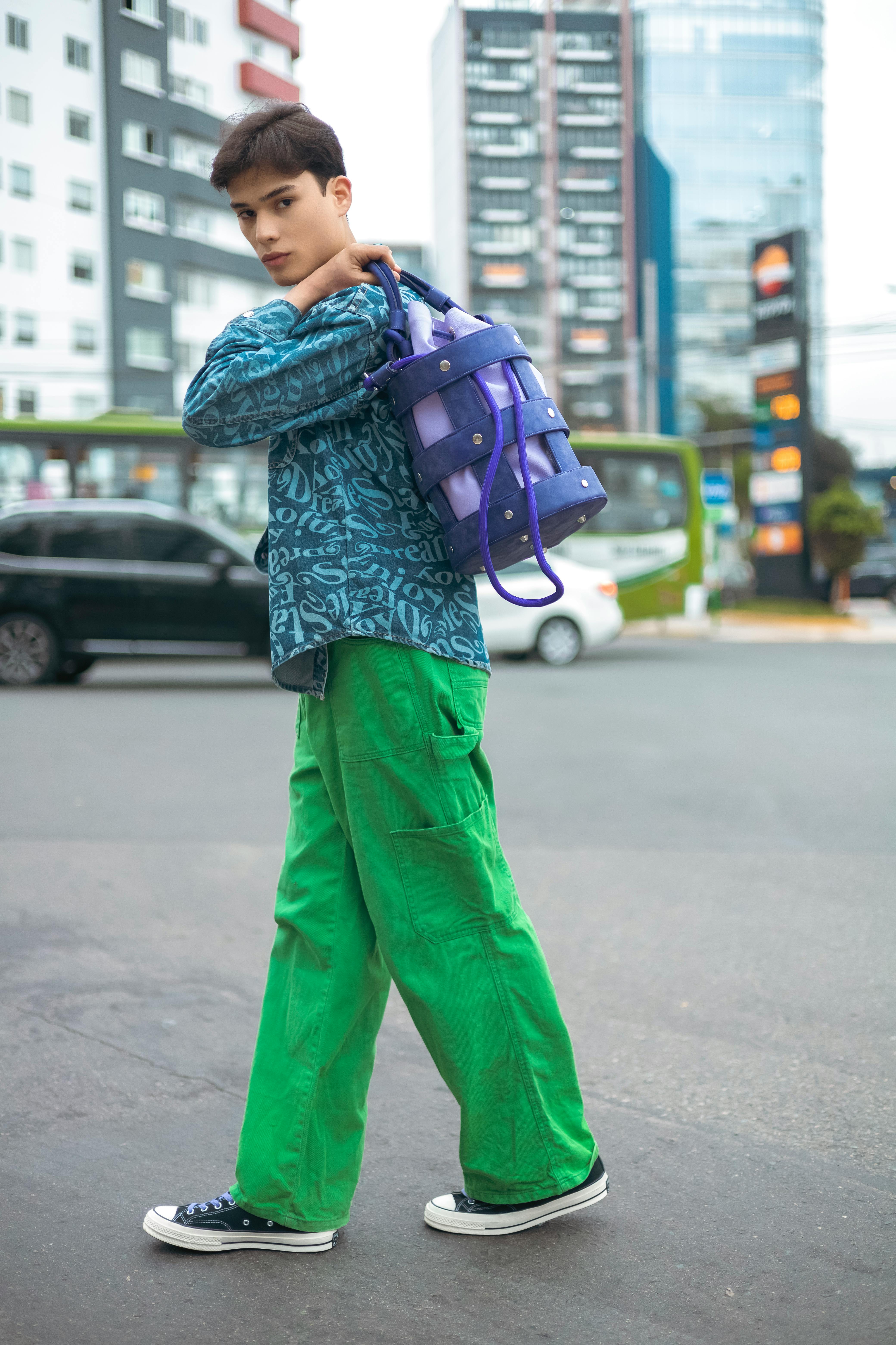 Free Model in green pants and patterned shirt posing on a city street with a stylish bag. Stock Photo