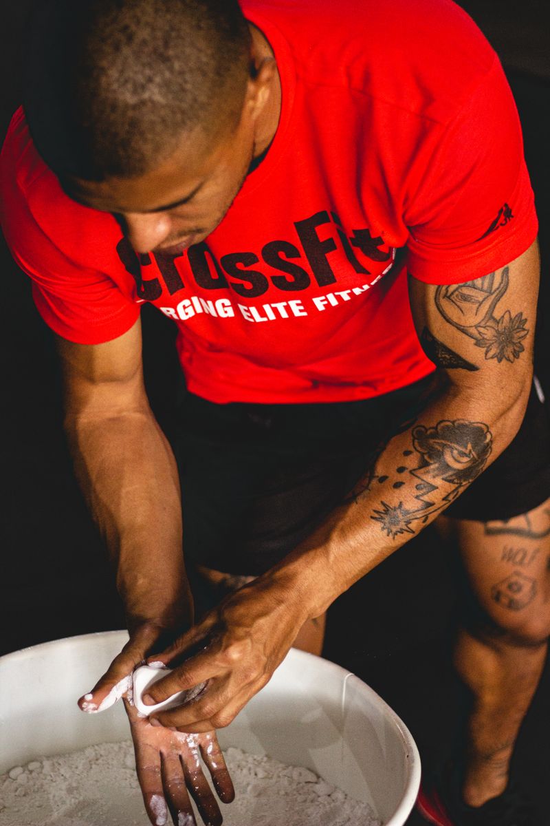 Atleta con camiseta roja echándose magnesio en las manos desde el cubo