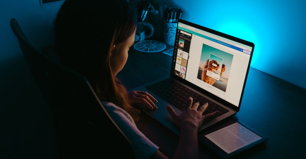 A girl uses a laptop at a desk in a dimly lit room, with a blue light creating a calm ambiance.