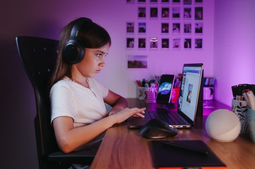 Free Girl with headphones using a laptop at her desk indoors, focused and engaged in a cozy atmosphere. Stock Photo