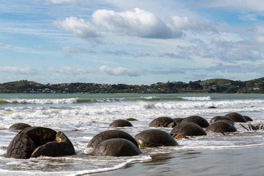 Moeraki Boulders on Koekohe Beach, New Zealand with waves crashing and a vivid sky.