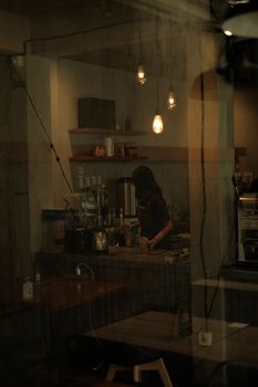 Warm café ambiance with barista preparing beverages, seen through a window.