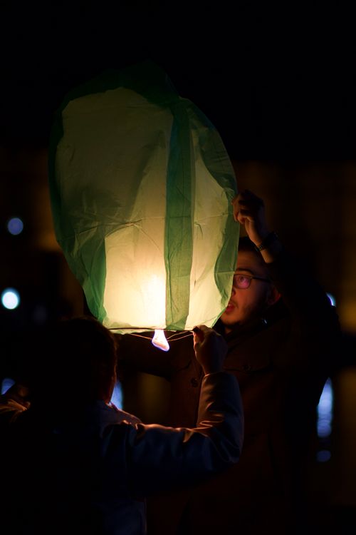 Free Two people release a glowing lantern into the night sky during a festive event. Stock Photo