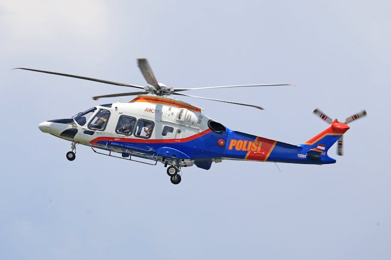 Dynamic view of a police helicopter flying through a clear blue sky, showcasing its design and vibrant colors.