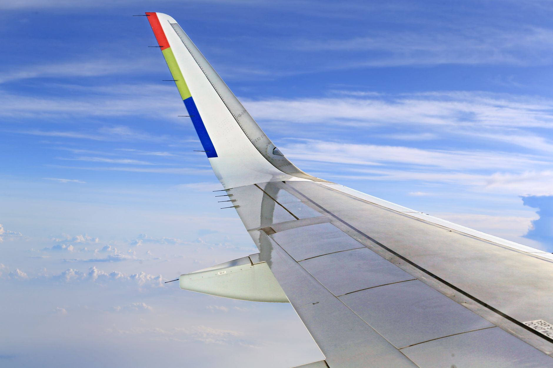 A stunning view of an airplane wing flying through a clear, cloud-speckled sky.