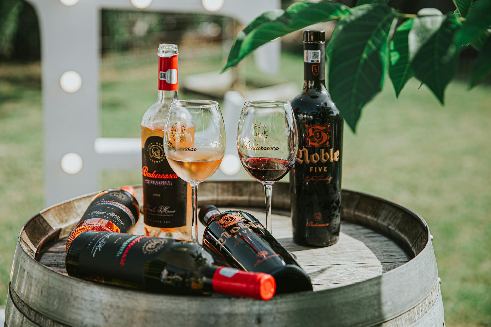 Rustic display of bottled wines and glasses on a wooden barrel in an outdoor setting.