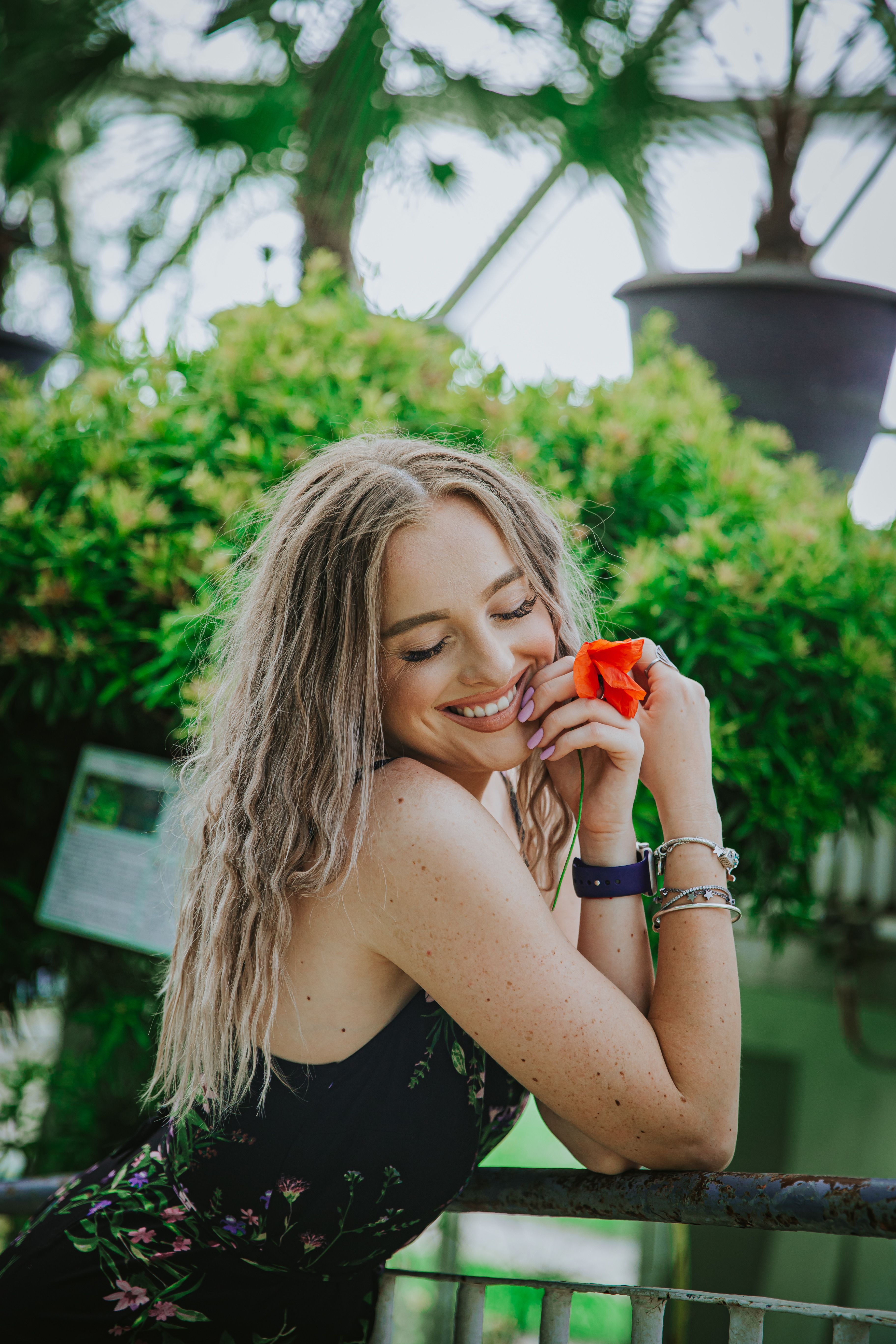 Smiling woman holding a flower in a lush green garden during summer.