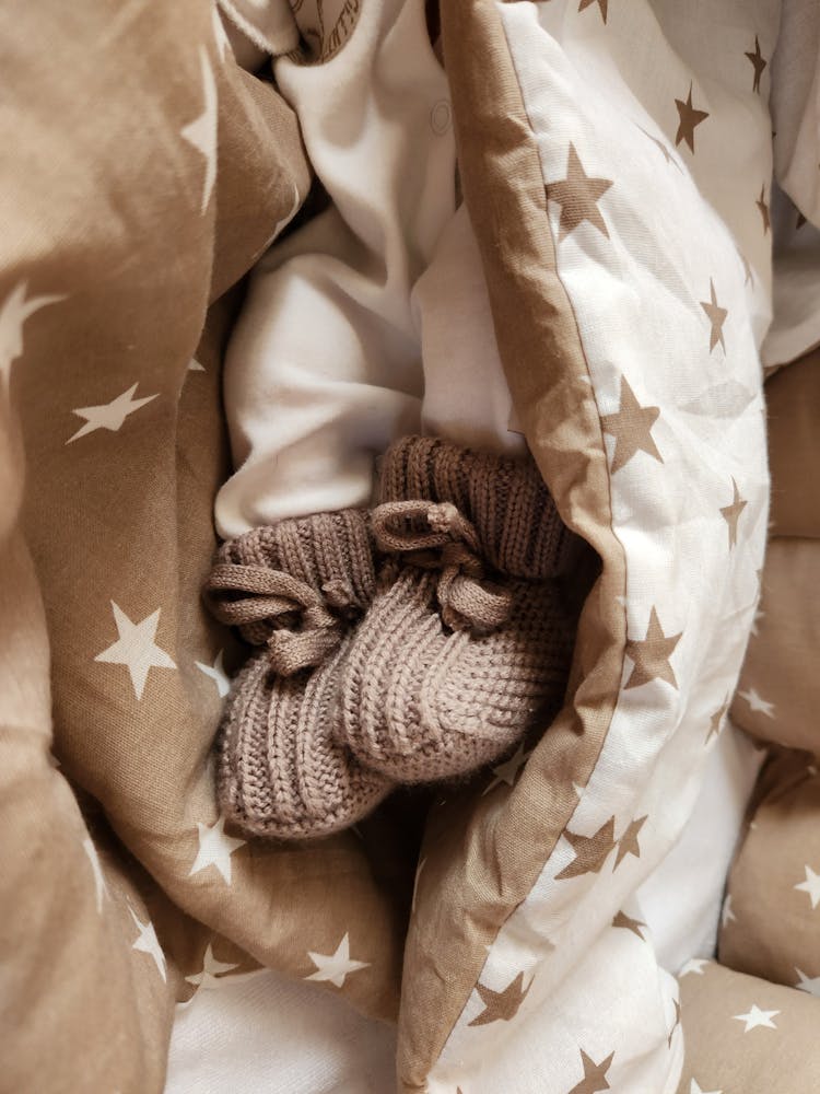 Newborn Baby Lying In Bed Wearing Crocheted Booties