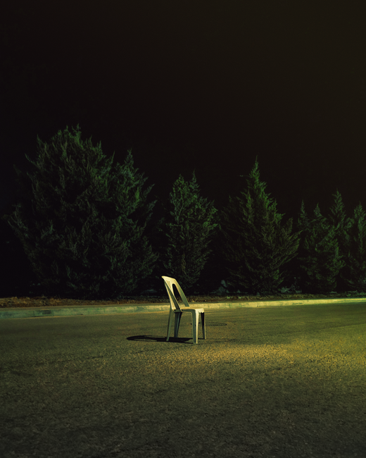 Single plastic chair under moody night sky with trees in background.