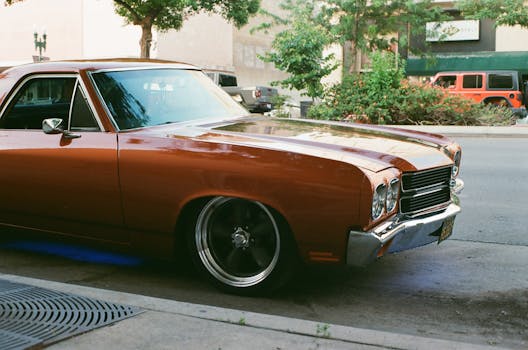 A classic brown Chevrolet El Camino parked on an urban street with trees and sidewalk.