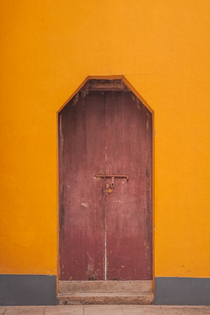 A vintage wooden door with a weathered lock against a bright yellow wall.