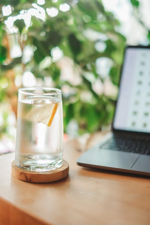 Glass of Water with Slice of Lemon by Laptop