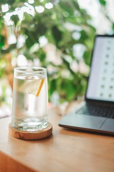 A glass of lemon water beside a laptop on a wooden table, creating a refreshing workspace atmosphere.