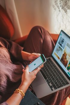 Relaxed person multitasking on smartphone and laptop in a cozy environment, combining work and leisure.