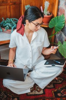 Adult woman multitasking with laptop and phone in a cozy home office setting.