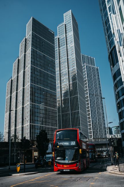 A classic view of London featuring towering skyscrapers and a red double-decker bus on a sunny day.
