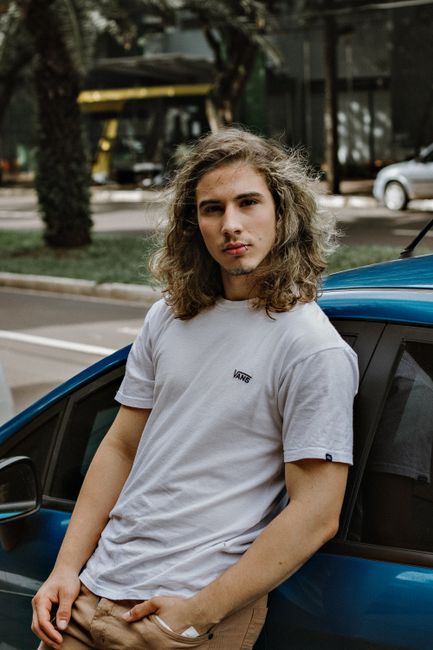 Casual portrait of a young man leaning on a car in a Brazilian city street, capturing urban style.