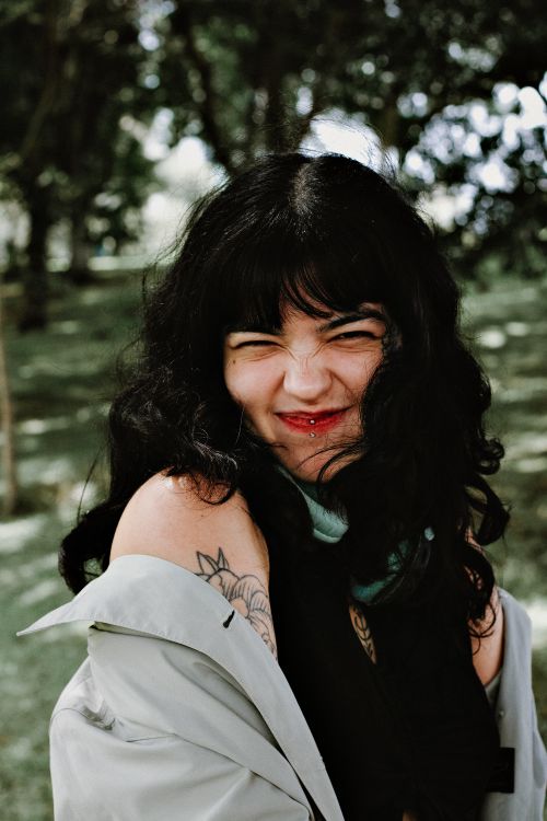 Free Playful portrait of a smiling woman with tattoos in a sunny park. Stock Photo
