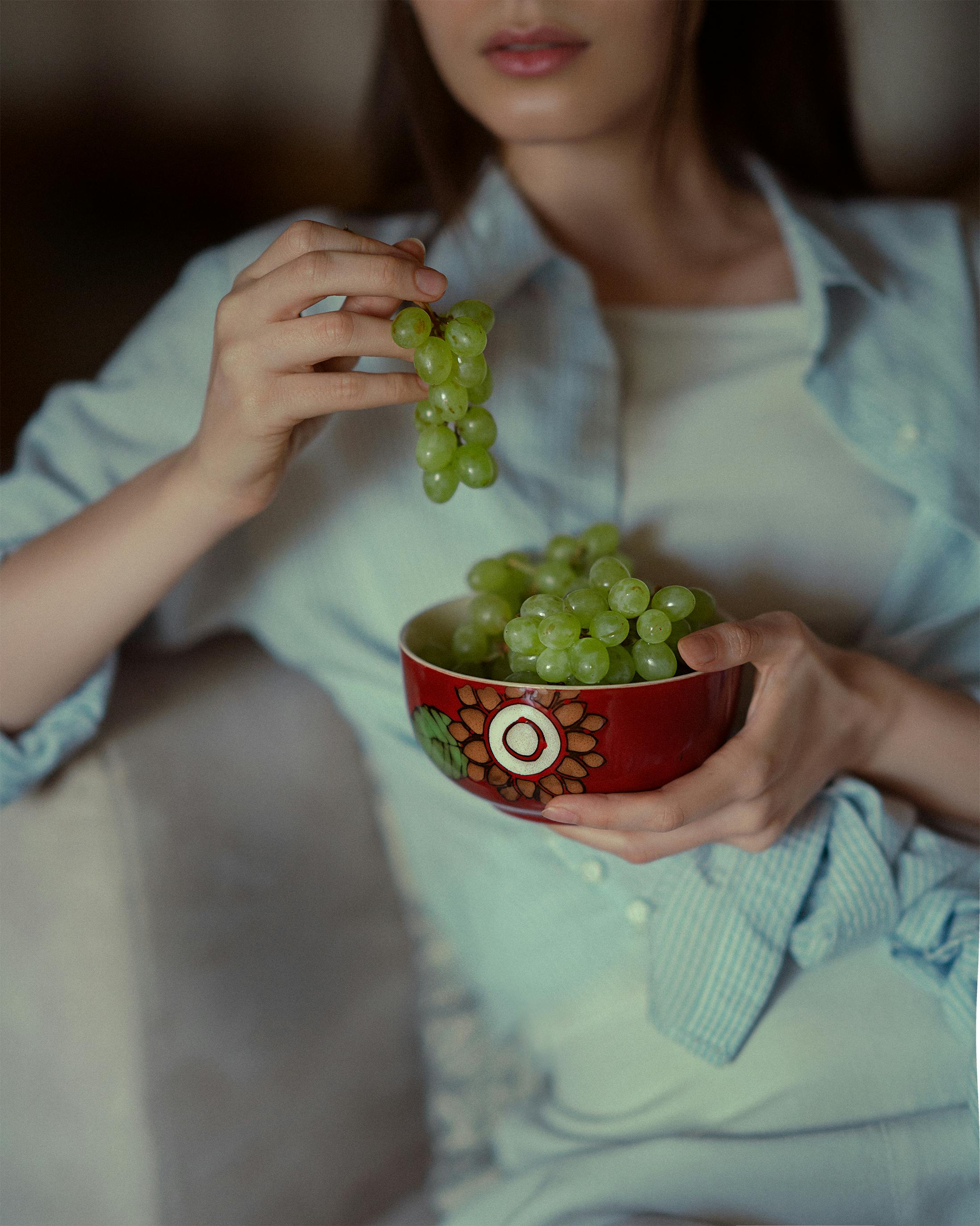 Close-up view of a woman holding a bowl of fresh green grapes indoors.