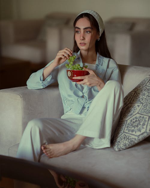 Free Woman Sitting on Couch and Eating Grapes Stock Photo