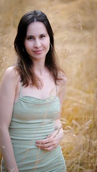 Portrait of a woman in a green dress posing in a golden field, embracing nature's elegance.
