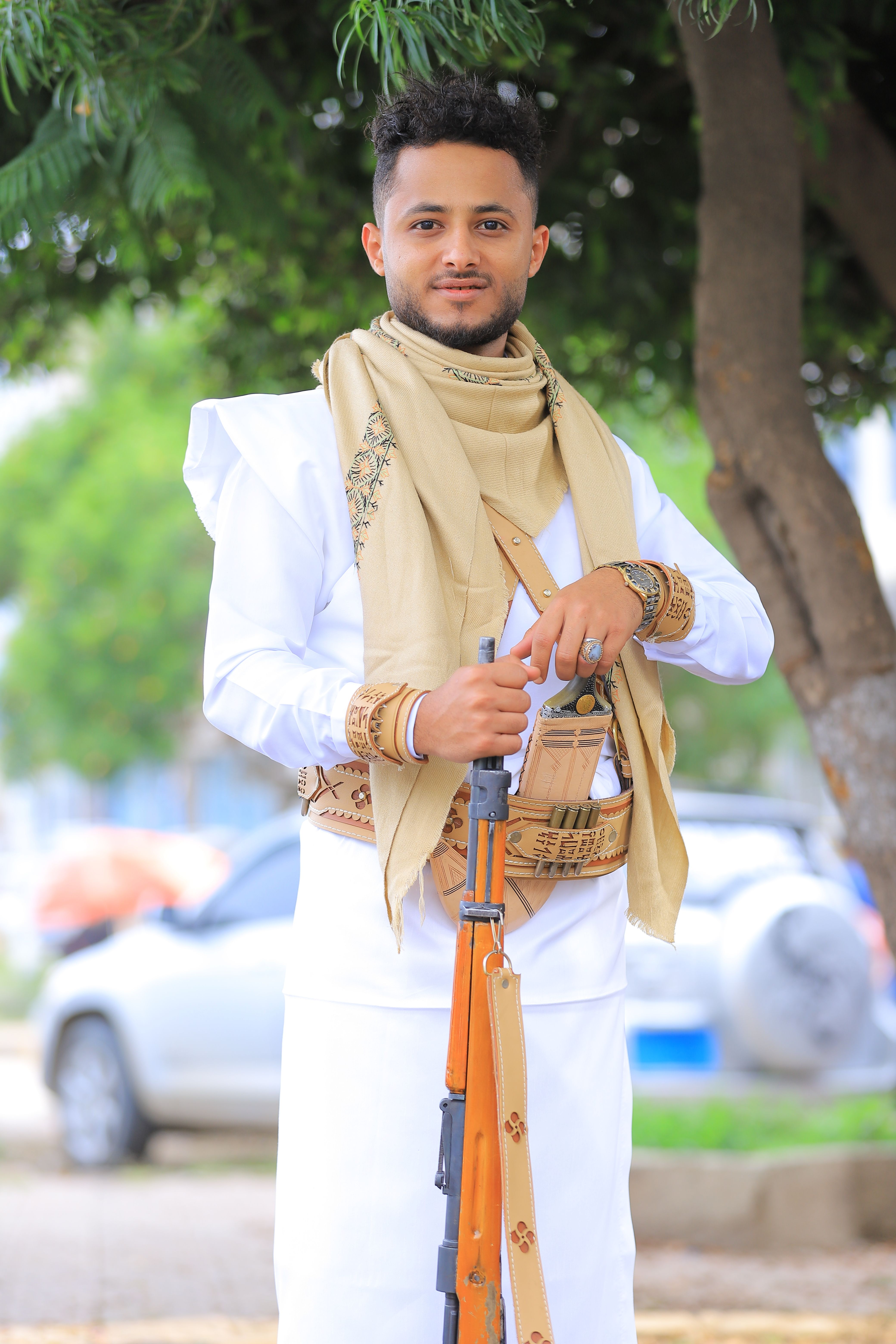 Portrait of a man in traditional attire with a rifle, outdoors with natural background.
