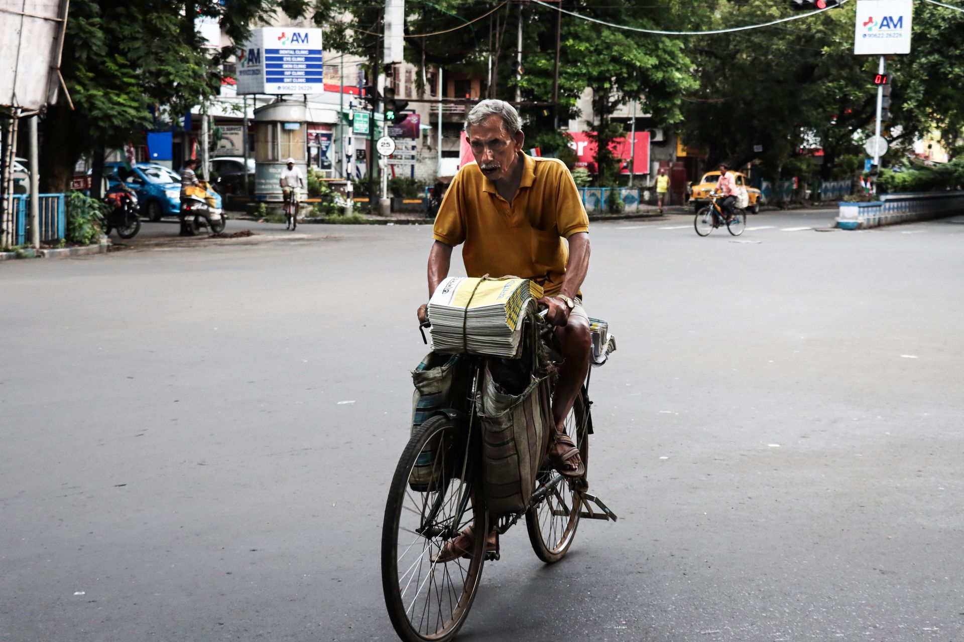 A man on a bicycle delivering newspapers in an urban city setting.