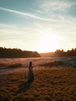 A woman stands in a misty field at sunrise, creating a serene and peaceful scene.