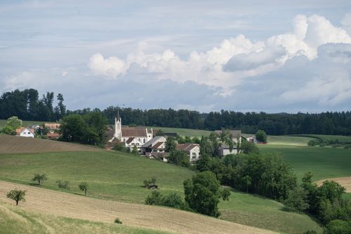 Free Picturesque rural village surrounded by lush green fields and rolling hills under a cloudy sky. Stock Photo