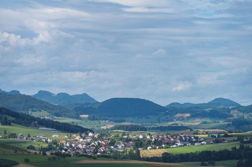 Free Picturesque rural village set against rolling hills and a vibrant countryside under a dramatic sky. Stock Photo