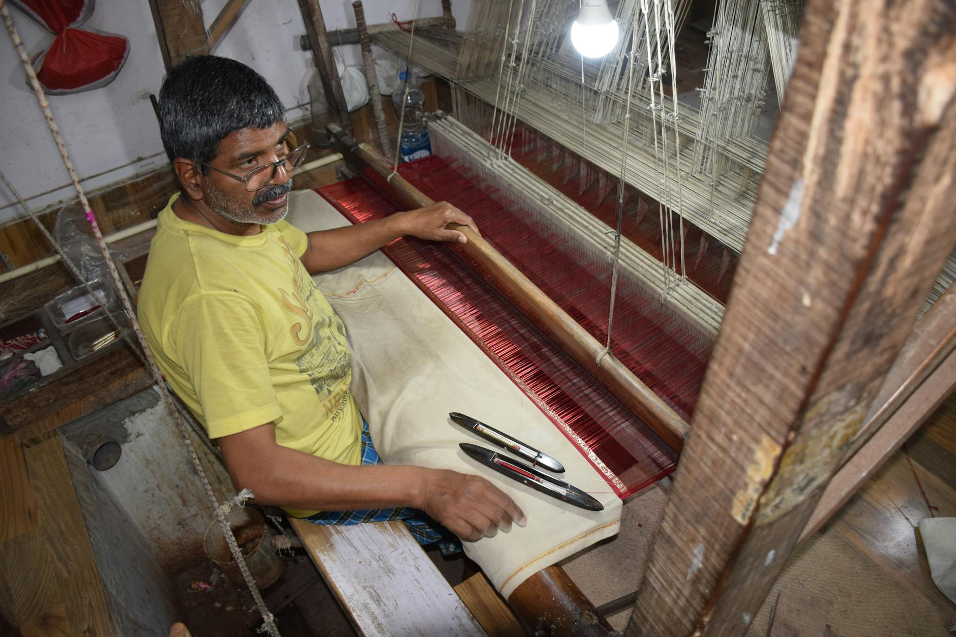 Elderly man weaving silk fabric using traditional methods in Varanasi workshop.