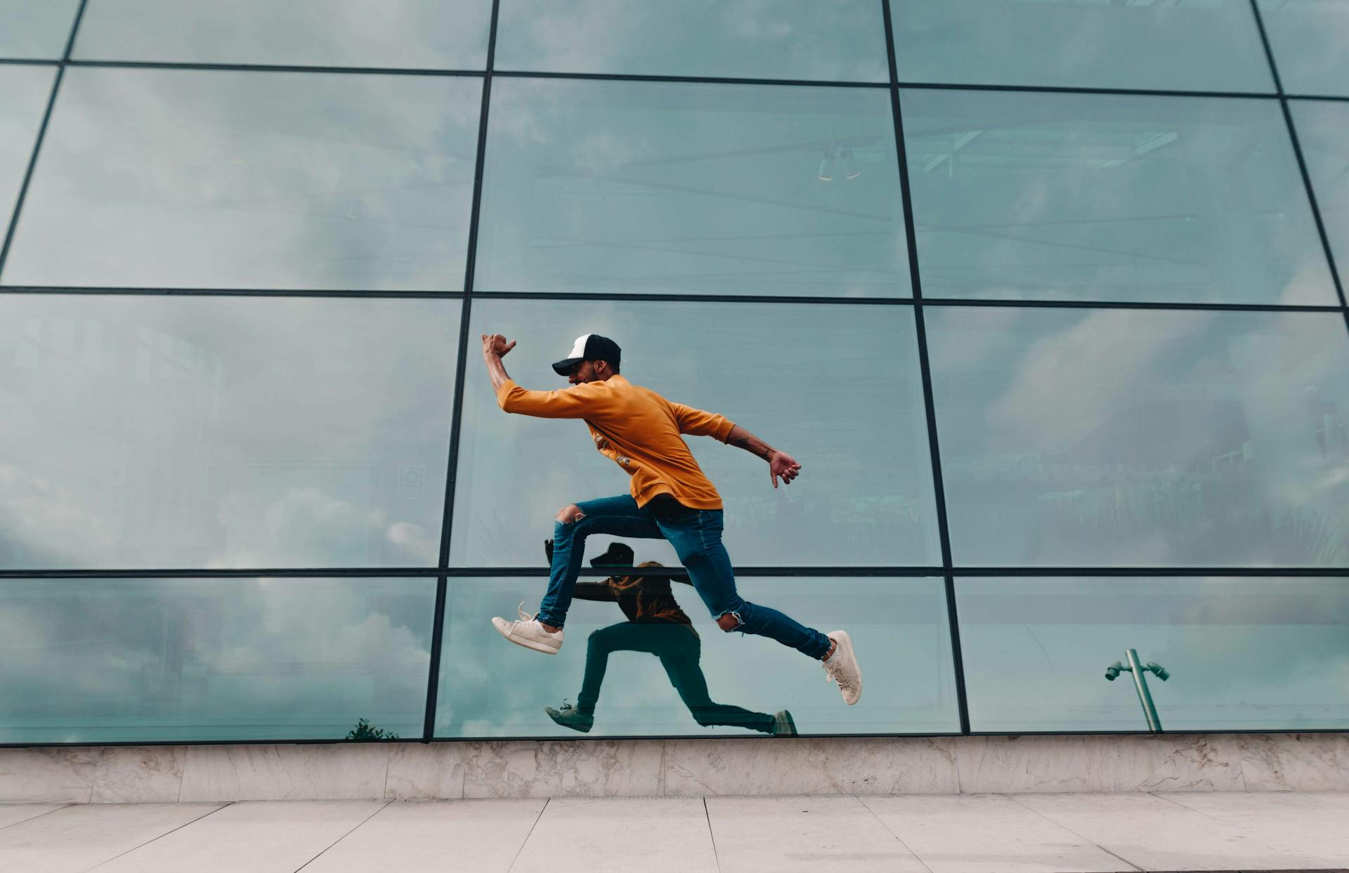 A man in motion jumps against a glass facade, creating a dynamic urban reflection.