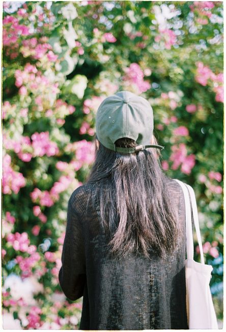 A woman in a cap stands before vibrant spring flowers, enjoying the colorful blooms.