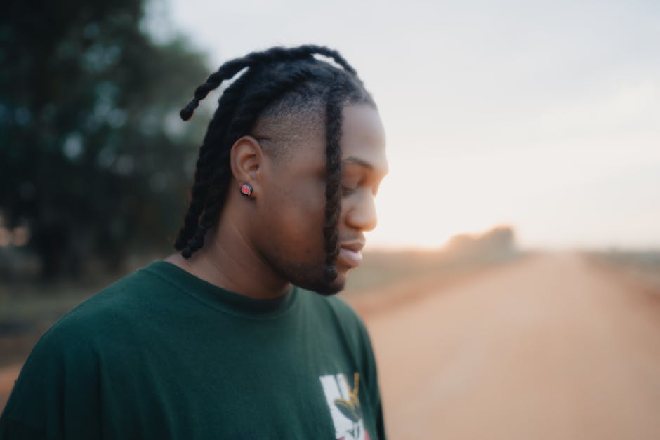 Tranquil profile portrait of a man with dreadlocks on a rural dirt road at sunset.