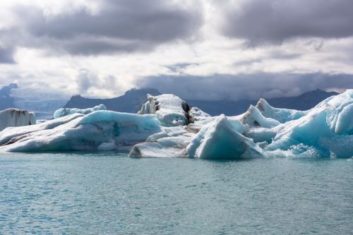 Free Stunning view of icebergs under cloudy sky, reflecting the beauty of untouched polar landscapes. Stock Photo