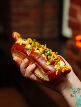 Close-up of a delicious gourmet hot dog with mustard and garnish in hand, perfect for fast food lovers.