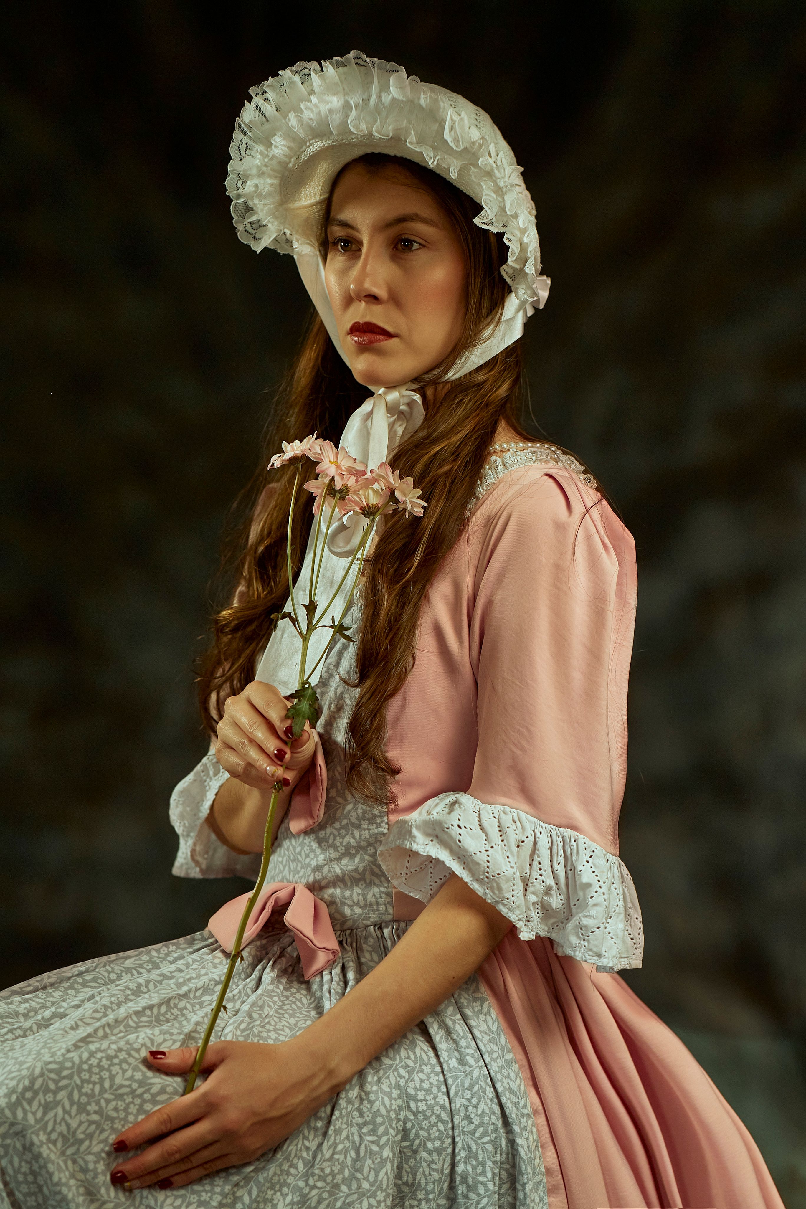A classic portrait of a woman posing in a vintage dress and hat, holding a flower.