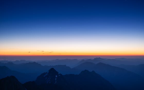 A breathtaking view of the Alps at sunrise with vibrant orange and blue hues over mist-covered peaks.