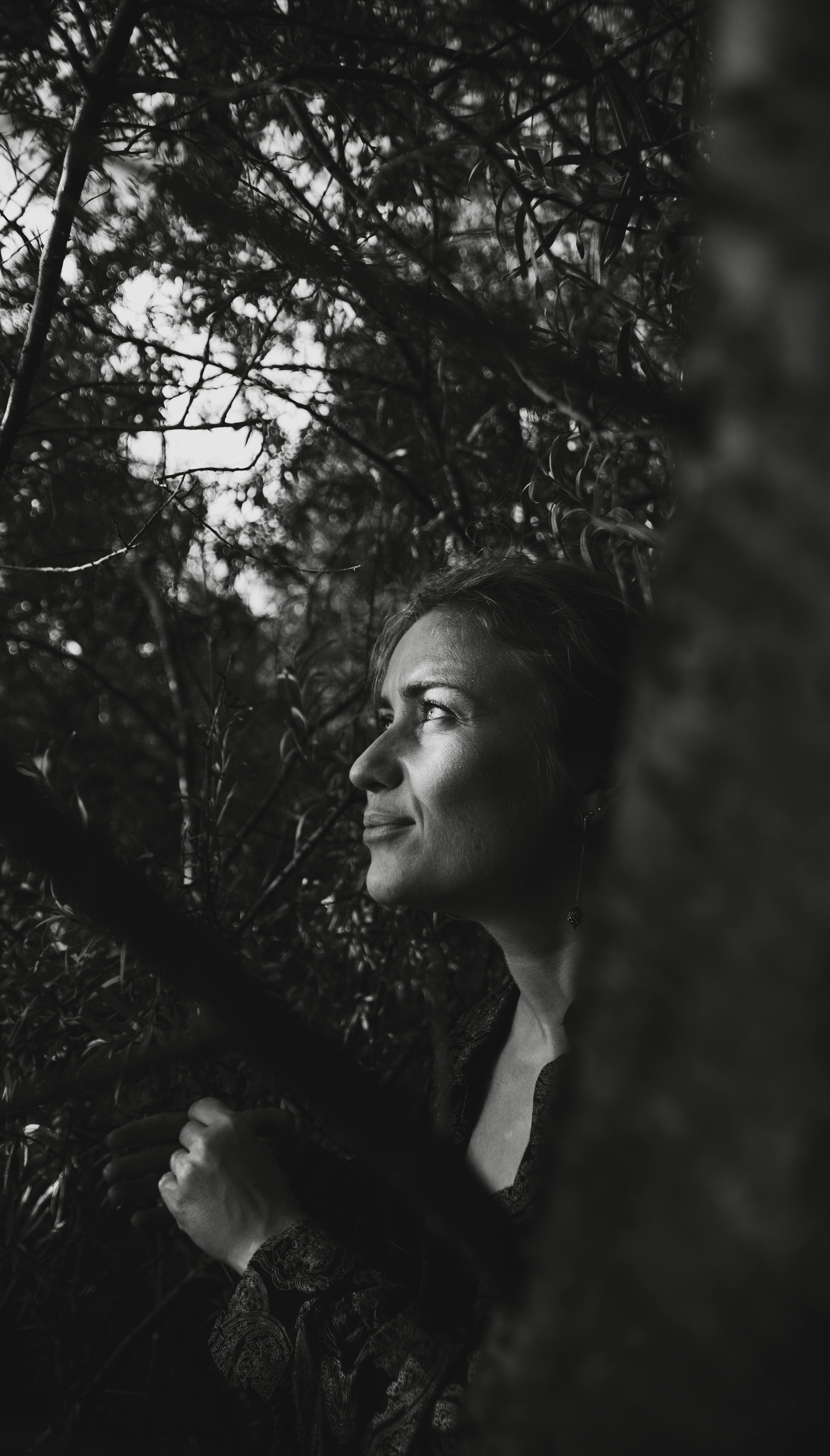 Black and white photo of a young woman looking up among trees in a forest.