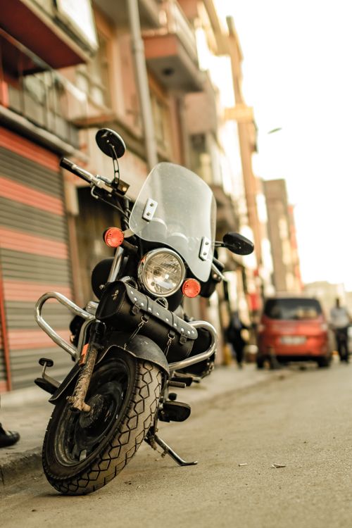 Free A close-up of a motorcycle parked on a city street, with urban buildings in the background. Stock Photo