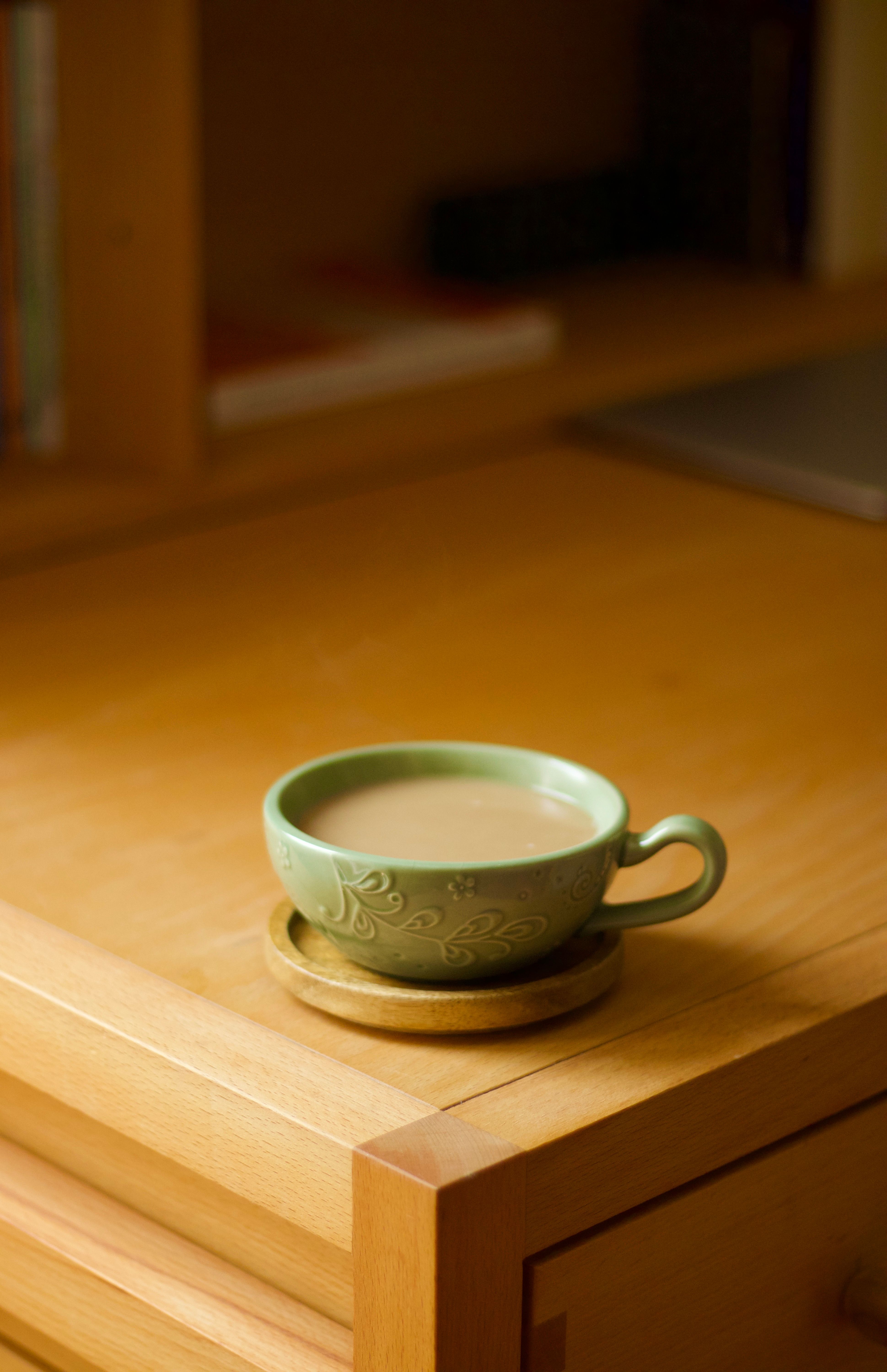 A warm cup of coffee in a green ceramic mug on a wooden table, captured in natural light.