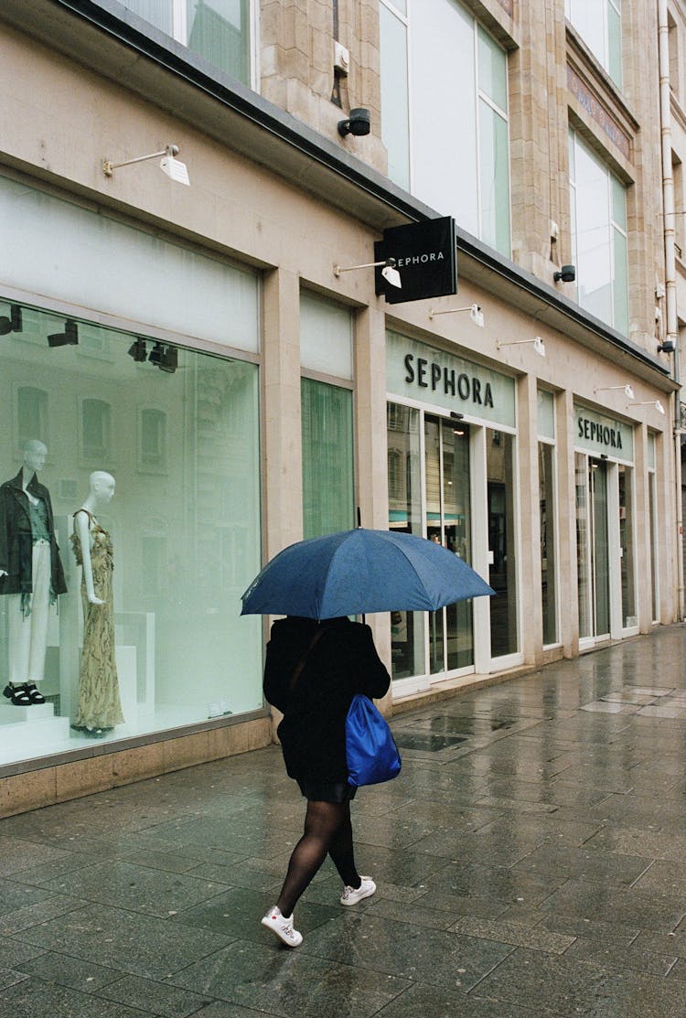 Woman With An Umbrella Walking Past The Stores In A City 