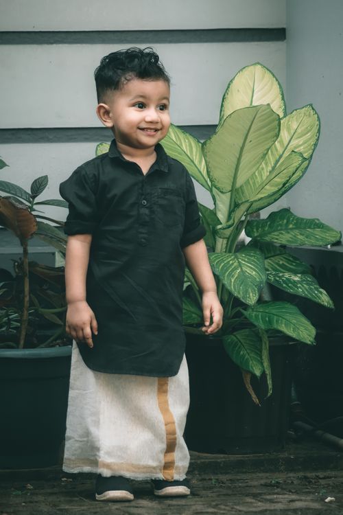 Free A cheerful child in traditional attire stands beside lush potted plants indoors. Stock Photo