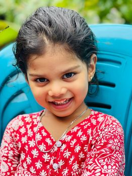 A cheerful young girl smiles in a red floral dress outdoors, showcasing joy and innocence.