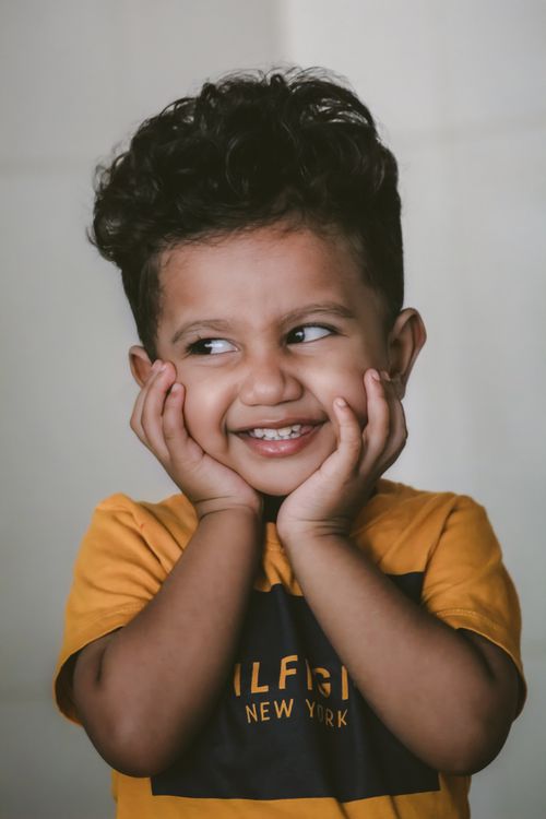 Free Charming portrait of a smiling toddler with hands on cheeks in a yellow t-shirt. Stock Photo
