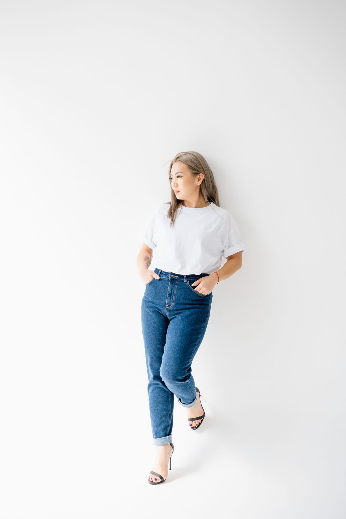 A woman in a white tee and blue mom jeans standing against a plain wall