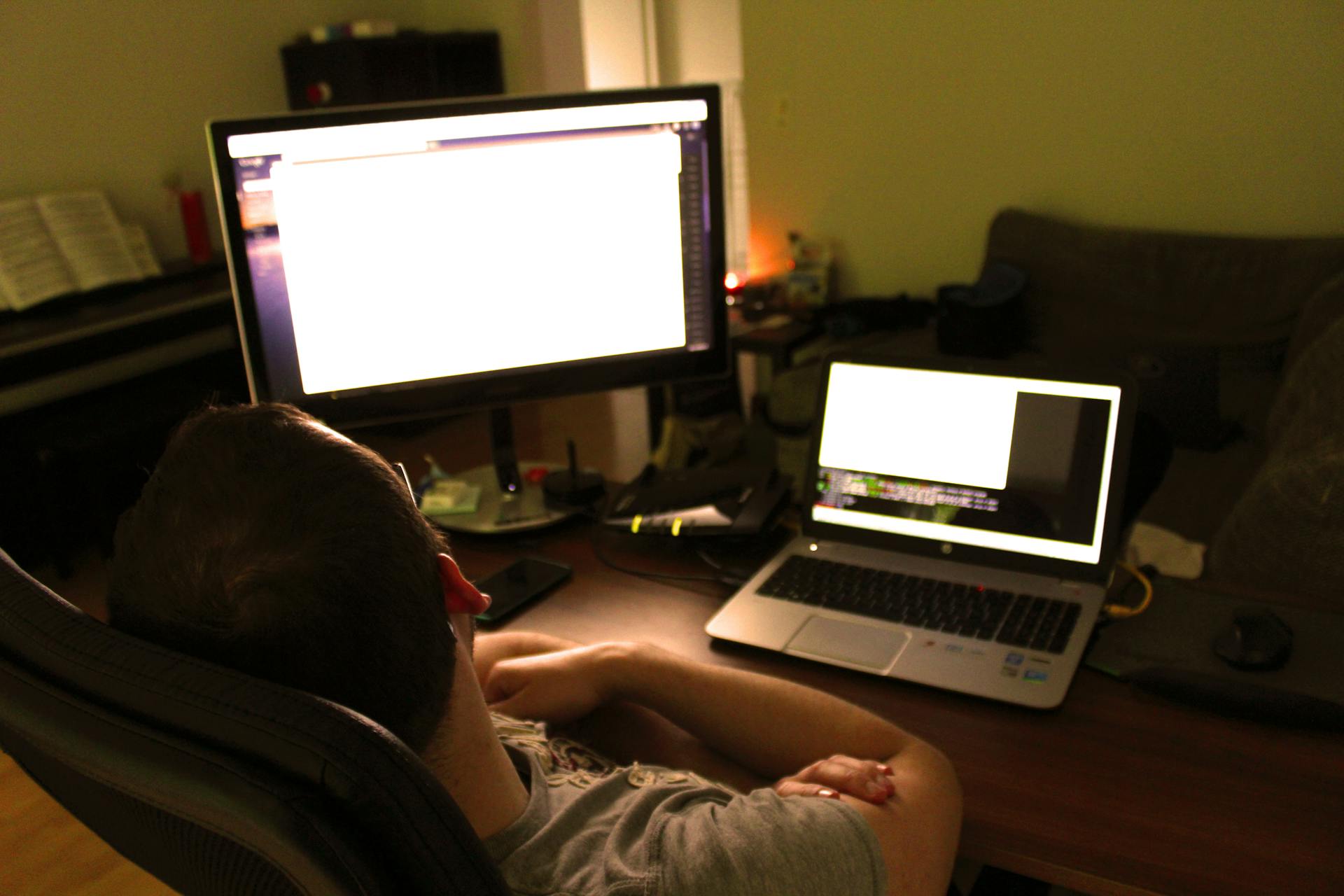 A man sitting at a desk working on a laptop and desktop, embodying modern remote work setup.